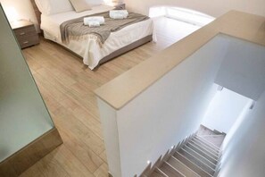 A bedroom with a bed, bedside tables, and a staircase.