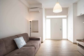 Una sala de estar moderna con un sofá, una lámpara colgante y una puerta que da a otra habitación.