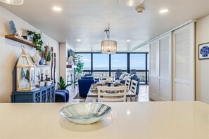 A spacious room with a dining area, a large window offering a view of the ocean, and a balcony with a railing. - Gulf Shores 203 Gorgeous 2nd Floor Beachfront View Private Balcony (Port Aransas)