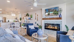 A modern living room with a fireplace, blue sofas, a dining area, and a kitchen in the background. - Gulf Shores 203 Gorgeous 2nd Floor Beachfront View Private Balcony (Port Aransas)