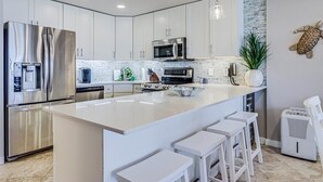 A modern kitchen with white cabinets, stainless steel appliances, and a central island with bar stools. - Gulf Shores 203 Gorgeous 2nd Floor Beachfront View Private Balcony (Port Aransas)