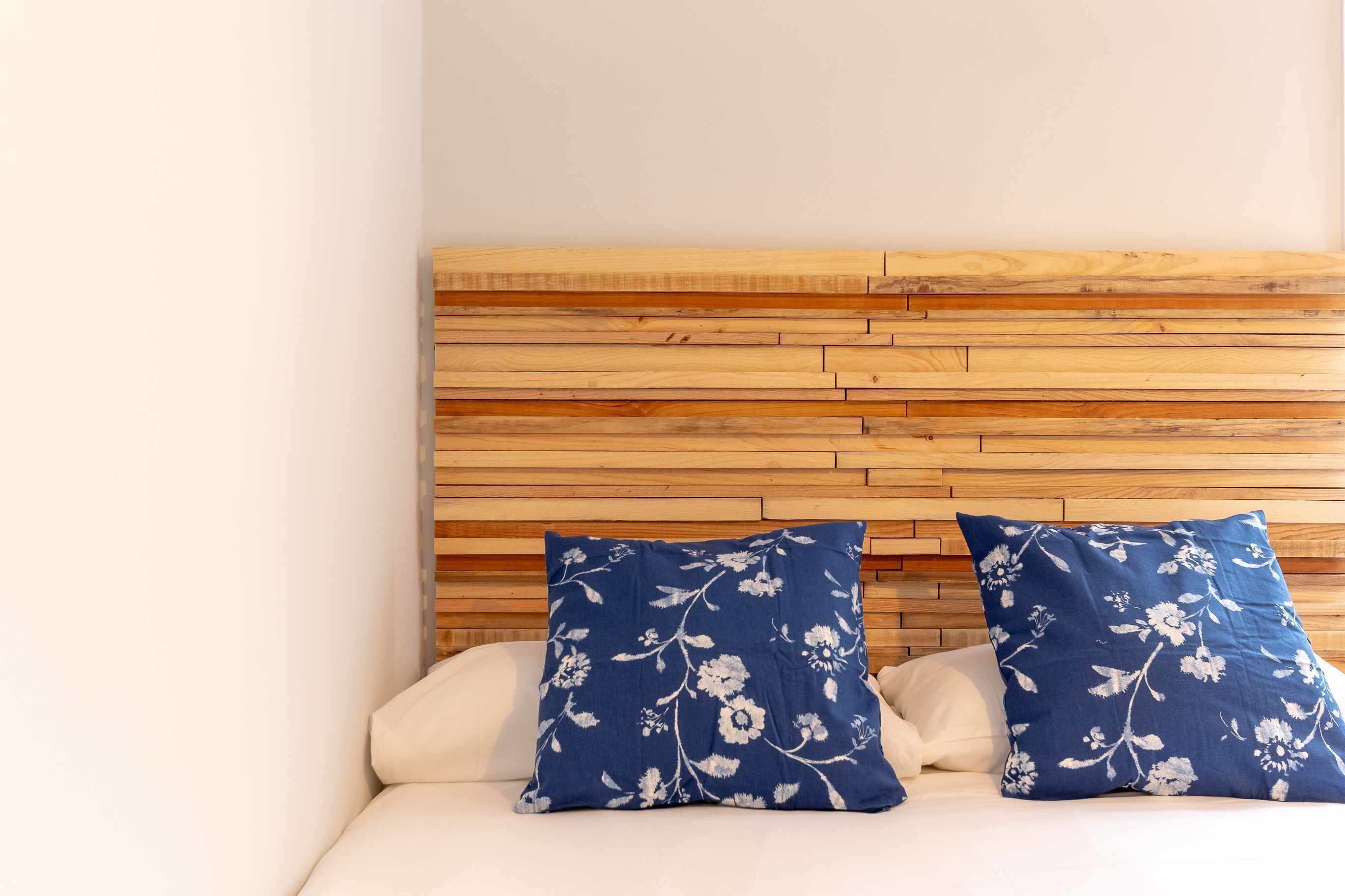Un lit avec une tête de lit en bois et deux coussins à motifs floraux bleus.