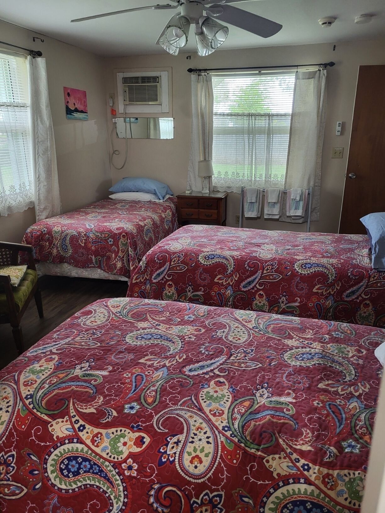 A bedroom with two beds, a ceiling fan, an air conditioning unit, and a window with curtains.