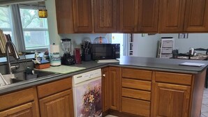 A kitchen with wooden cabinets, a microwave, a dishwasher, and a window with a view of trees.