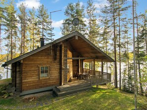 Een houten chalet met een veranda, schoorsteen en een schotelantenne.