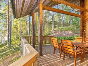A wooden deck with a table and chairs, surrounded by a forest.