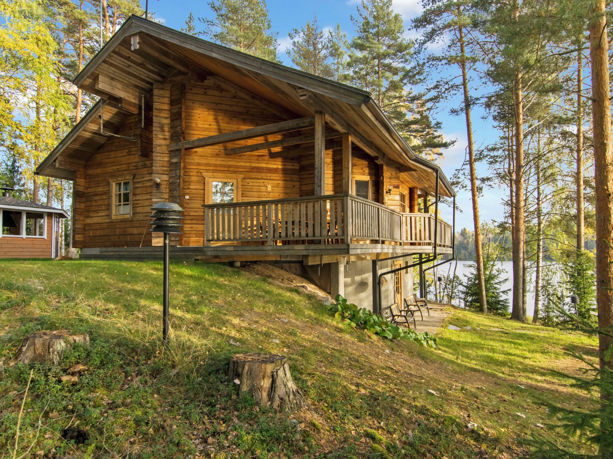 Une cabane en bois dotée d’un balcon, située sur une colline et offrant une vue sur un lac et une forêt.