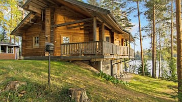 Une cabane en bois dotée d’un balcon, située sur une colline et offrant une vue sur un lac et une forêt.