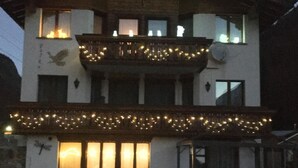 A two-story building with a balcony, string lights, and a bird mural. - Haus Falke by Interhome (Saas-Grund)