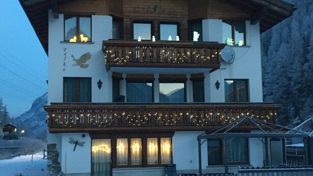 A two-story building with a wooden balcony, a mountain backdrop, and snow on the ground. - Haus Falke by Interhome (Saas-Grund)