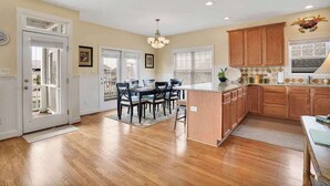 A kitchen with wooden cabinets, a dining area with chairs, and a central island. - Doin` Time by Brunswick Vacation Rentals: 5BR Ocean View Home w/ Dock & Elevator (Ocean Isle Beach)