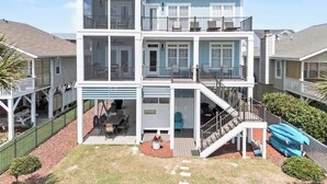 A multi-story residential building with a covered patio, outdoor seating, and a staircase leading to the upper levels. - Doin` Time by Brunswick Vacation Rentals: 5BR Ocean View Home w/ Dock & Elevator (Ocean Isle Beach)