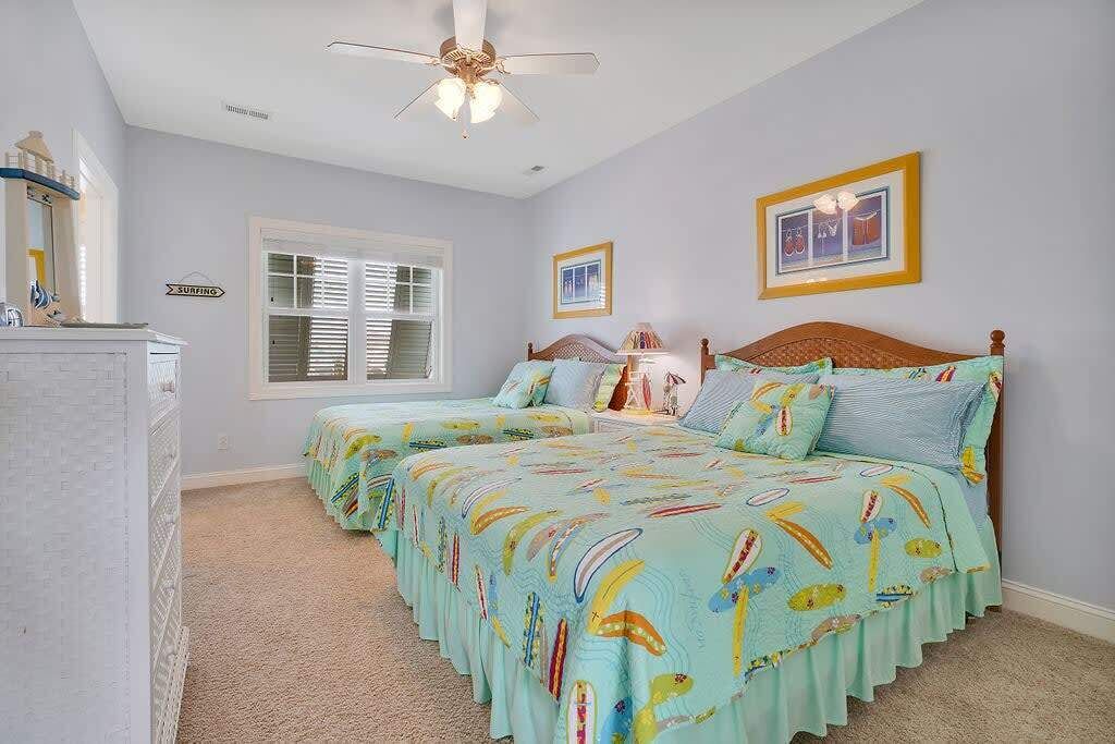 A bedroom with two beds, a ceiling fan, a window with blinds, and a framed picture on the wall.