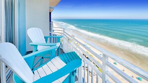A balcony with turquoise chairs overlooking a beach.