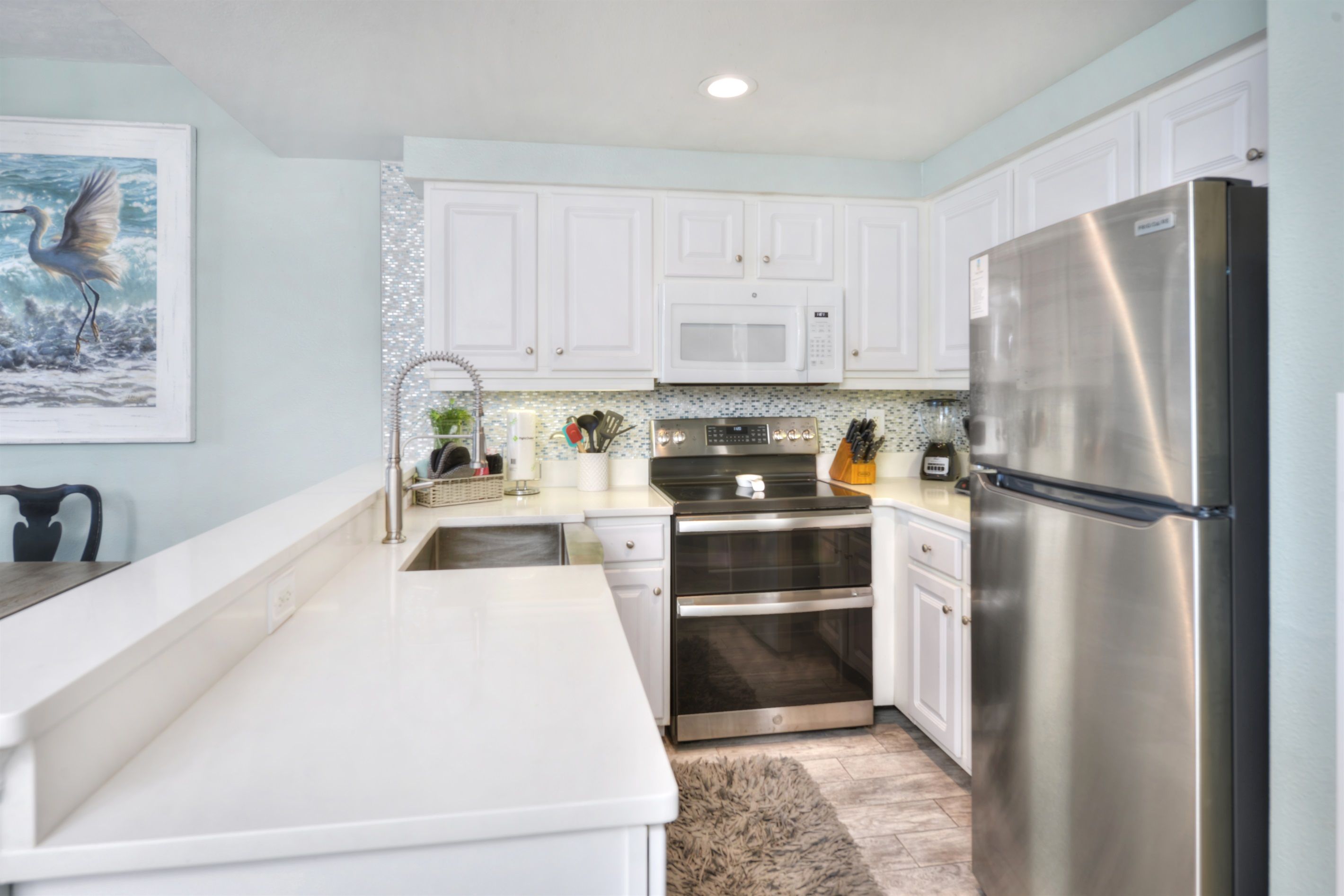 A modern kitchen with white cabinets, stainless steel appliances, and a marble countertop.