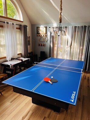 Une table de ping-pong avec deux raquettes et une balle, une table en bois recouverte d’une nappe blanche et une chaise.