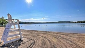 A beach chair with a sign, a sandy beach, and a calm lake with a clear sky.