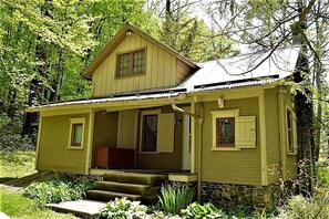 A two-story house with a porch, stone foundation, and a metal roof.