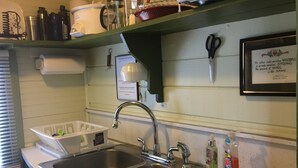 Una cucina con due lavelli in acciaio inossidabile, un espositore per piatti e diversi oggetti da cucina sul piano di lavoro e sugli scaffali.