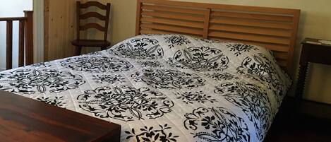 A bedroom with a wooden bed frame, a white and black patterned bedspread, a wooden nightstand, and a framed picture on the wall.