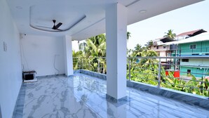 Uma varanda ampla com piso de mármore, ventilador de teto e vista para uma área residencial com palmeiras e edifícios.