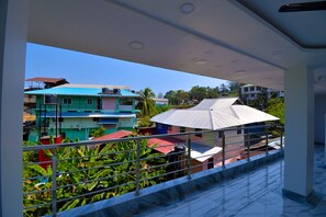 Un balcon doté d’une rambarde en métal, donnant sur un quartier résidentiel avec des bâtiments aux couleurs vives et une végétation luxuriante.
