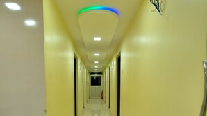 Um corredor longo e bem iluminado, com paredes amarelas e pisos brancos, que leva a uma porta no final.