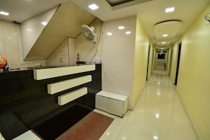 Un espace d’accueil comprenant un comptoir de réception, un ventilateur, un panneau indiquant « Réception » et un couloir menant à une porte.