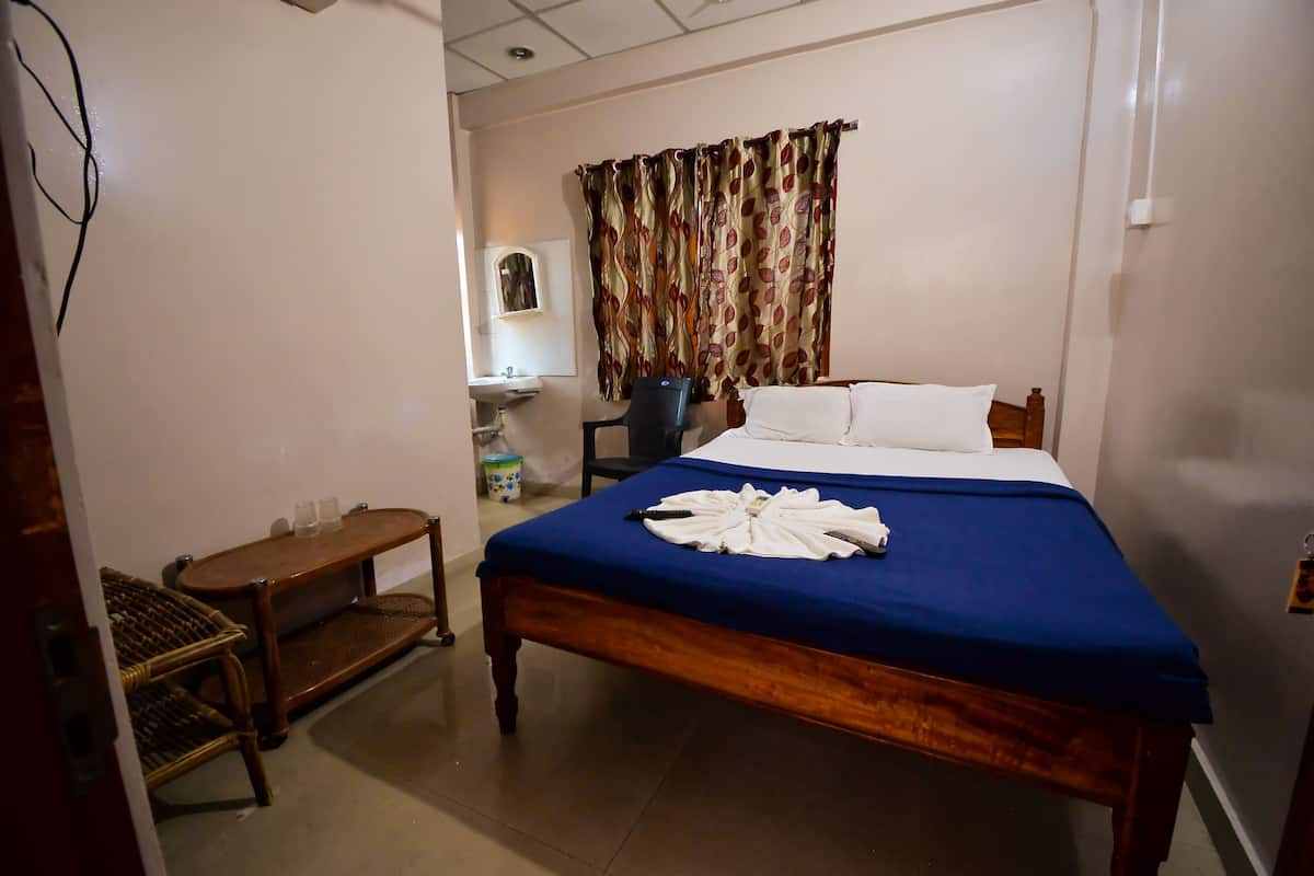 A bedroom with a bed, a bedside table, a chair, a small table, a sink, and a curtain.