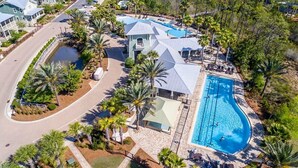 Oversigtsbillede af et resort med en stor swimmingpool, flere gæstevillaer og velholdt natur med palmer.