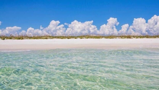 En strand med klart, lavt vand og en hvid sandstrand.