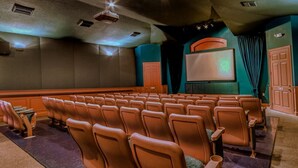 A movie theater with rows of brown seats, a screen, and a projector.