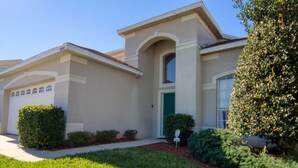 A single-story house with a garage, a green door, and a small front yard with trimmed bushes.