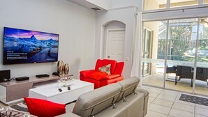 A modern living room with a flat-screen TV, a red sofa, a grey sofa, and a white coffee table.