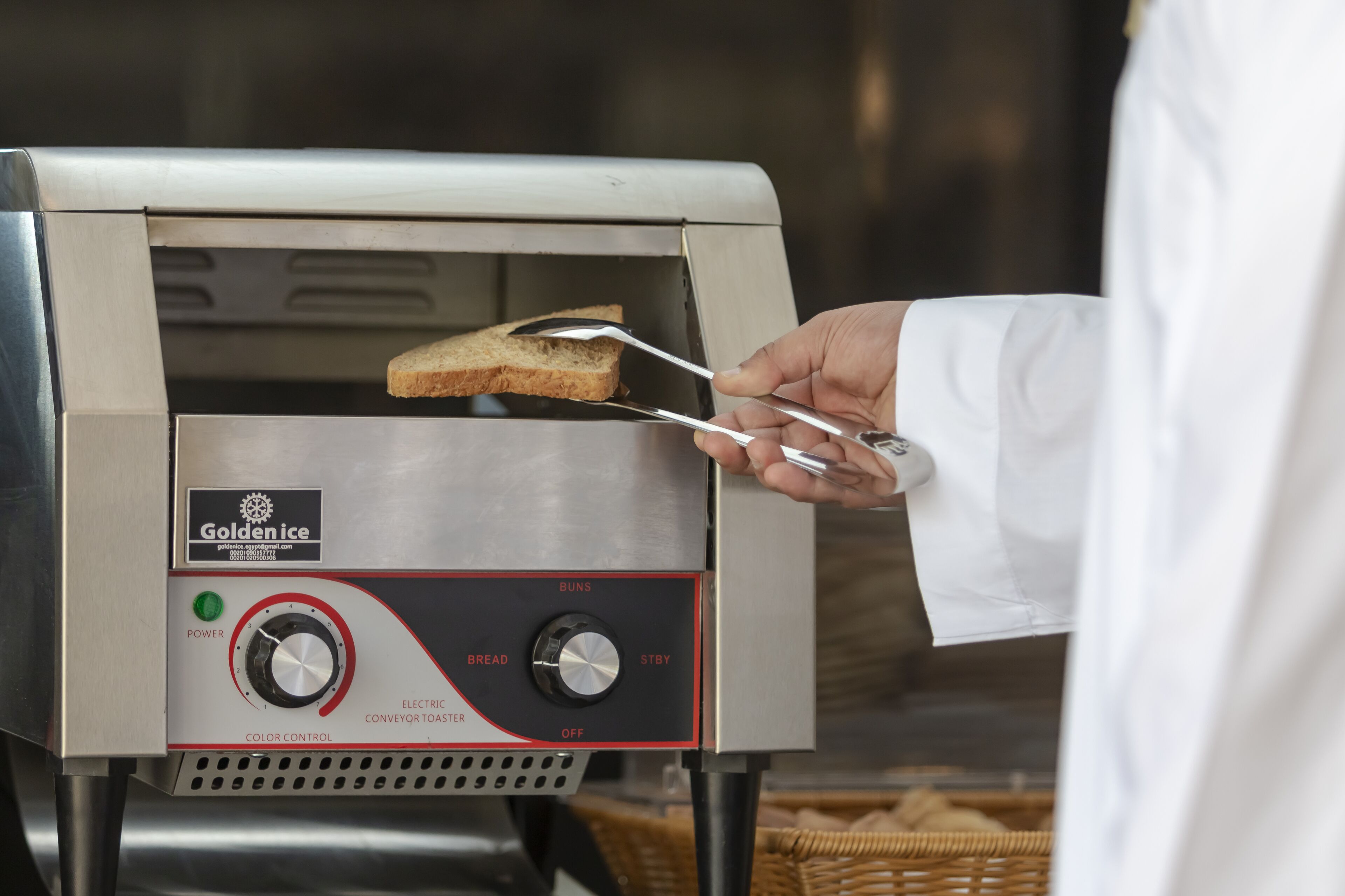 A person using tongs to place a slice of bread into a toaster oven.