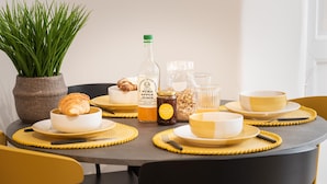 Une table à manger dressée avec des sets de table jaunes, une bouteille de jus de pomme, un pot de miel et un croissant.