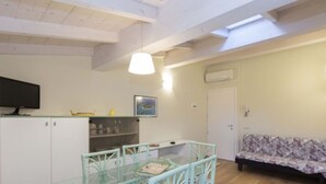 Ein Zimmer mit Esstisch, Stühlen, einer Couch, einem Fernseher und einer Decke mit Oberlicht.