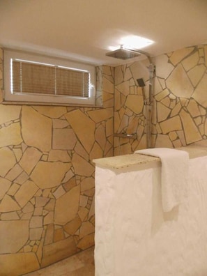 A bathroom with a stone wall, a shower, and a window with blinds.