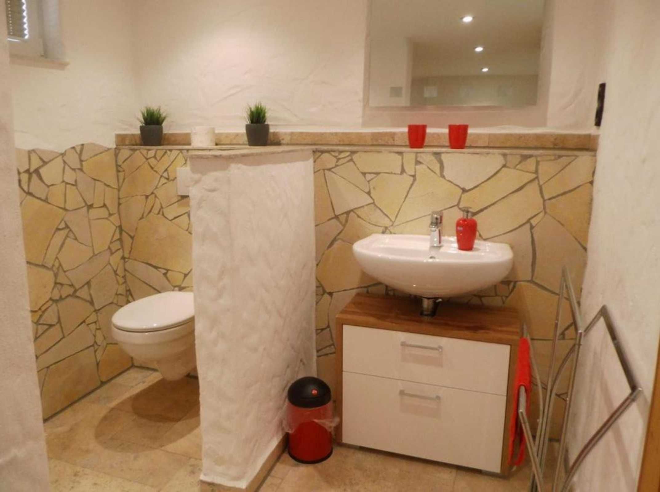Ein Badezimmer mit Steinwand, Toilette, Waschbecken mit Spiegel und einem kleinen Schrank.