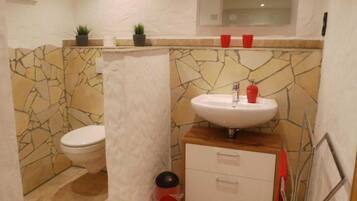 Ein Badezimmer mit Steinwand, Toilette, Waschbecken mit Spiegel und einem kleinen Schrank.