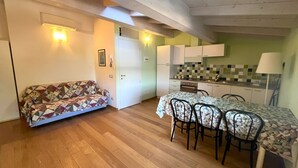 Ein gemütliches Zimmer mit einer Couch, einem Esstisch mit Stühlen, einer Küchenzeile und einer Tür zu einem weiteren Raum.