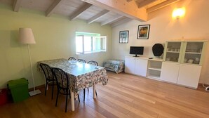 Ein Zimmer mit Esstisch, Stühlen, Fernseher, Schrank und Fenster.