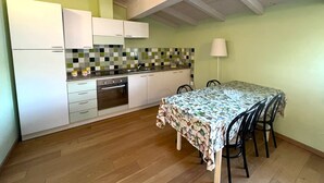 Eine kompakte Küche mit weißen Schränken, einer gefliesten Spritzschutzwand und einem Essbereich mit einem Tisch, der mit einer gemusterten Tischdecke bedeckt ist.