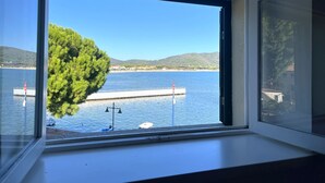Ein Zimmer mit großem Fenster mit Blick auf ein Gewässer, eine Anlegestelle und einen Baum.
