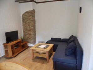 Ein Wohnzimmer mit Fernseher, einer Couch, einem Couchtisch und einer Ziegelwand.