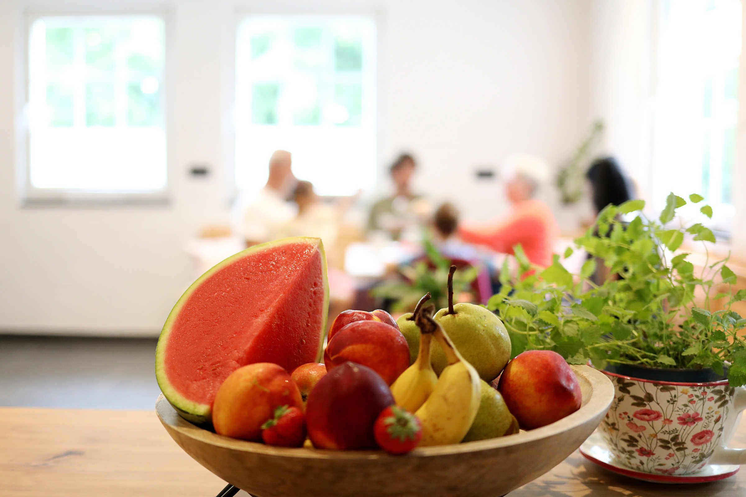 Eine Schale Obst auf einem Tisch, daneben ein Blumentopf.