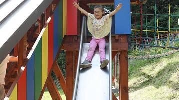 A child sliding down a metal slide with a wooden structure and colorful panels.