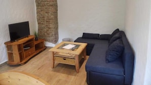 Una sala de estar con televisor, sofá, una mesa de centro y una pared de ladrillo.