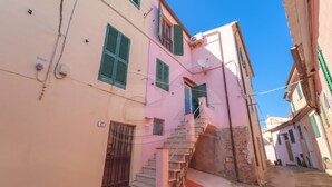 A narrow street with a pink building featuring a staircase leading to a second floor. - NEL CUORE DI RIO MARINA (Rio Marina)