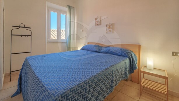 A bedroom with a bed, a bedside table, a hanging clothes rack, and a window with curtains. - NEL CUORE DI RIO MARINA (Rio Marina)